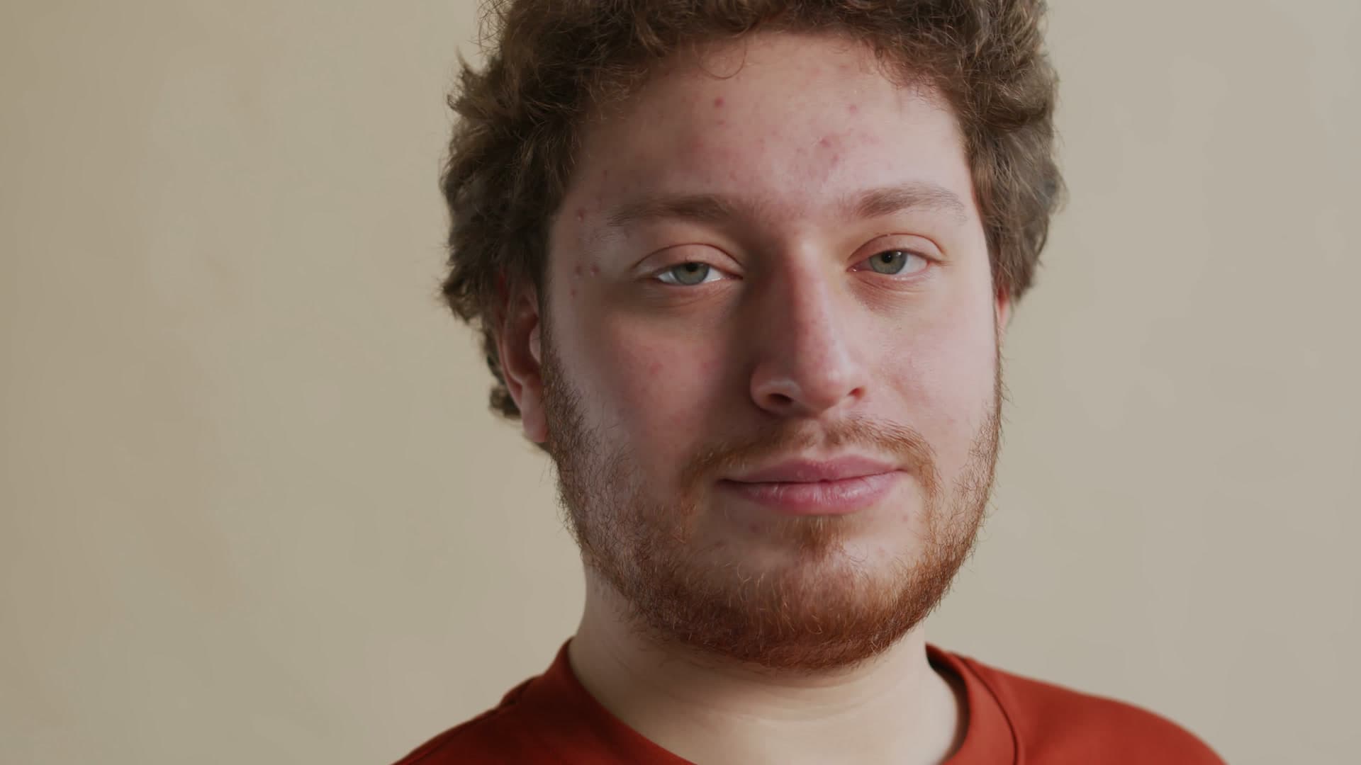 Curly-haired man against a beige wall in sharp 1080p